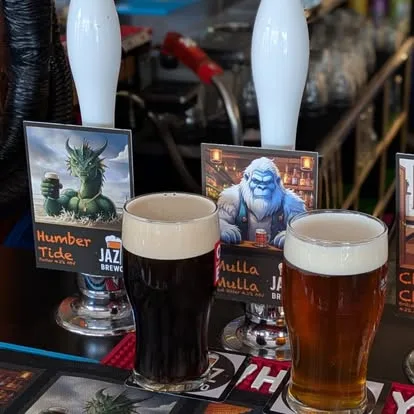 Two freshly poured pints, a dark Humber Tide and an amber ale, with Jazz BrewCo pump clips lined up behind